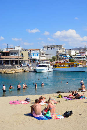 Tourists in the sea and on the beach with views of the harbour and town, Sissi, Crete, Greece, Europe.のeditorial素材