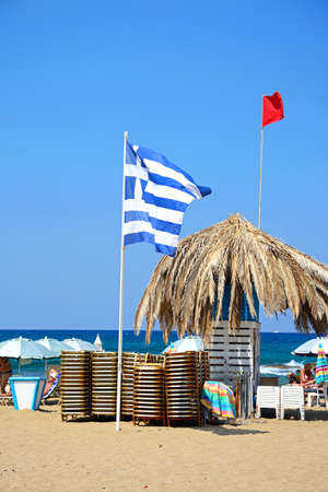 Flags, sun loungers and a large parasol on Potamos beach with the sea to the rear, Malia, Crete, Greece, Europe.のeditorial素材