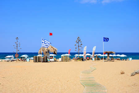 View of Potamos beach with flags and parasols and the sea to the rear, Malia, Crete, Greece, Europe.のeditorial素材