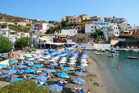 Tourists relaxing on the beach with town buildings to the rear, Bali, Crete, Greece, Europe.のeditorial素材