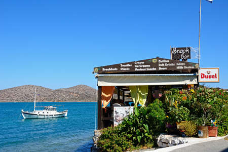 Greek taverna along the waterfront with a boat moored in the bay, Elounda, Crete, Greece, Europe.のeditorial素材