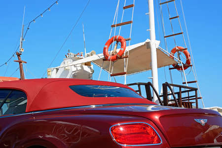 Red soft topped Bentley Continental car with a yacht to the rear, Elounda, Crete, Greece, Europe.