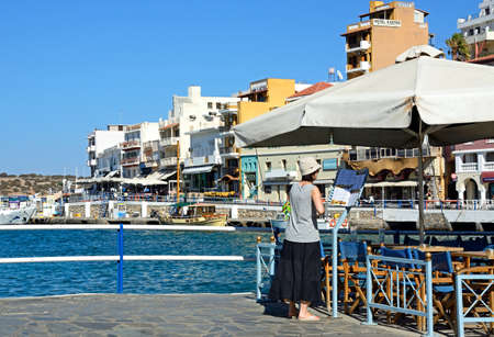 Tourists looking at a restaurant menu along the harbour waterfront, Agios Nikolaos, Crete, Greece, Europe.のeditorial素材