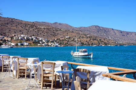 Restaurant tables on the waterfront with views across the bay, Elounda, Crete, Greece, Europe.のeditorial素材