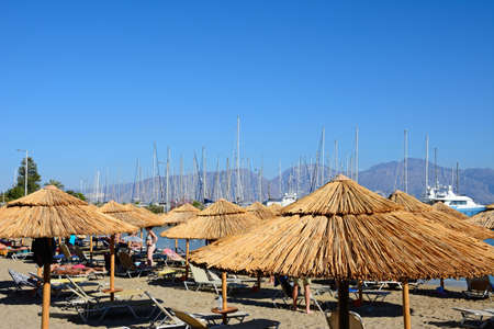 Tourists relaxing on the beach with views towards the marina, Agios Nikolaos, Crete, Greece, Europe.のeditorial素材