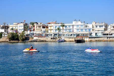 Man riding a jetski in the harbour with views towards waterfront restaurants, Hersonissos, Crete,...