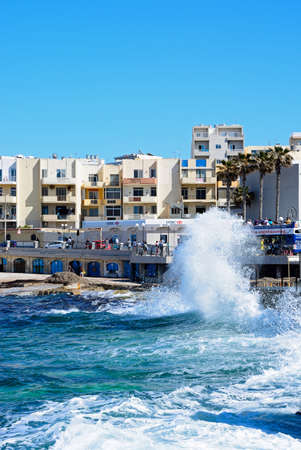 Sea crashing onto the rocky coastline with a shopping street to the rear, Bugibba, Malta, Europe.のeditorial素材