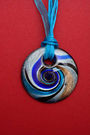 Blue round glass Maltese pendant against a red background