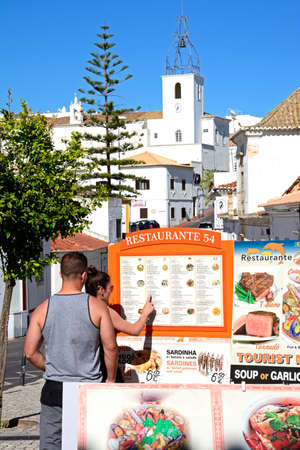 A young couple looking at a menu board outside a restaurant in the old town, Albufeira, Algarve, Portugal, Europe.のeditorial素材