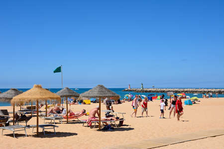 Tourists relaxing on the beach with views towards the harbour entrance breakwaters, Vilamoura, Algarve, Portugal, Europe.のeditorial素材