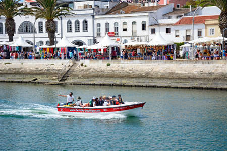 Tourists aboard small tour boats along the river Bensafrim with views towards the promenade and municipal market, Lagos, Algarve, Portugal, Europe.のeditorial素材