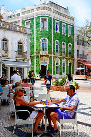 Tourists relaxing at pavement cafes in the Praca Luis de Camoes with a green tiled traditional Portuguese building to the rear, Lagos, Algarve, Portugal, Europe.のeditorial素材