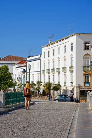 Young woman walking across the Roman bridge with town buildings to the rear, Tavira, Algarve,...