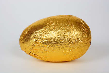 Chocolate Easter egg wrapped in gold foil against a white background, UK.