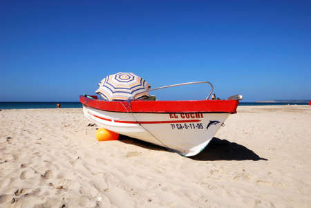 ZAHARA DE LOS ATUNES, SPAIN - SEPTEMBER 14, 2008 - Traditional red and white wooden fishing boat on the beach with tourists enjoying the setting, Zahara de los Atunes, Cadiz Province, Andalusia, Spain, Europe, September 14, 2008.のeditorial素材