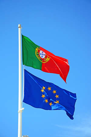 Portuguese and European Union Flags flapping against a blue sky, Praia da Monte Gordo; Vila Real de Santo Antonio, Algarve, Portugal, Europe.の写真素材