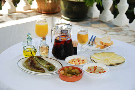 A selection of tapas with a jug of Sangria, beer and orange juice, Fried pointed green peppers, Green olive cocktail, Cubed Manchego cheese with chilli, Pickled cucumber with chilli, and sliced Manchego cheese, Costa del Sol, Malaga Province, Andalucia, Spain, Western Europe.の写真素材