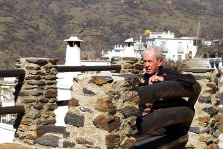 Elderly Spanish man sitting on a bench on a viewing platform overlooking the town, Bubion, Spain.のeditorial素材