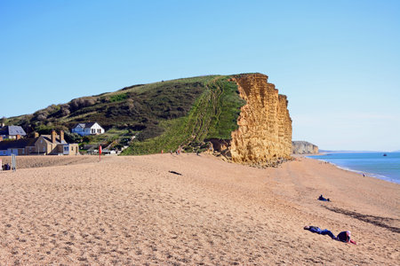 WEST BAY, UK - OCTOBER 10, 2022 - Tourists relaxing on the beach with views of the Jurassic Coast cliffs, West Bay, Dorset, UK, Europe, October, 2022.のeditorial素材