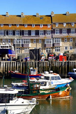 WEST BAY, UK - OCTOBER 10, 2022 - Fishing boats moored in the harbour with apartments to the rear, West Bay, Dorset, UK, Europe, October, 2022.のeditorial素材