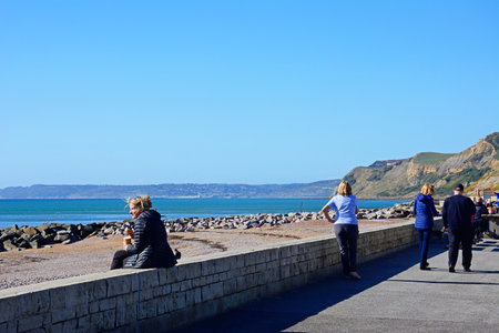 WEST BAY, UK - OCTOBER 10, 2022 - Tourists on the promenade with views of the beach and Jurassic Coast, West Bay, Dorset, UK, Europe, October, 2022.のeditorial素材