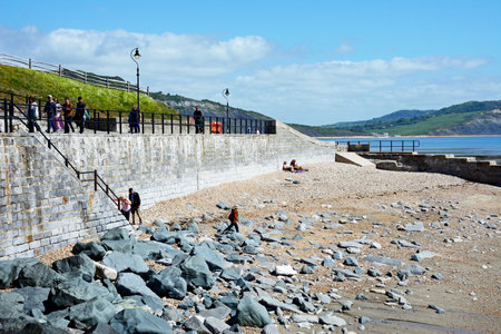 LYME REGIS, UK - MAY 14, 2022 - Tourists relaxing along the rocky beach with views towards The Spittles, Lyme Regis, Dorset, UK, Europe, May 14, 2022.のeditorial素材