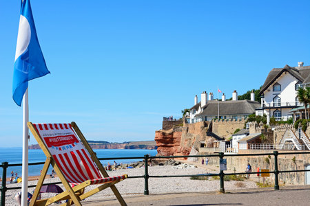 SIDMOUTH, UK - AUGUST 08, 2022 - View of traditional thatched houses overlooking the beach at the West End of the town with a large deckchair in the foreground, Sidmouth, Devon, UK, Europe, August 08, 2022.のeditorial素材