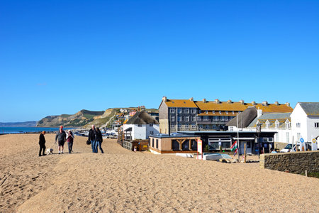 WEST BAY, UK - OCTOBER 10, 2022 - People walking along the pebble beach with views of the town and coastline, West Bay, Dorset, UK, Europe, October, 2022.のeditorial素材