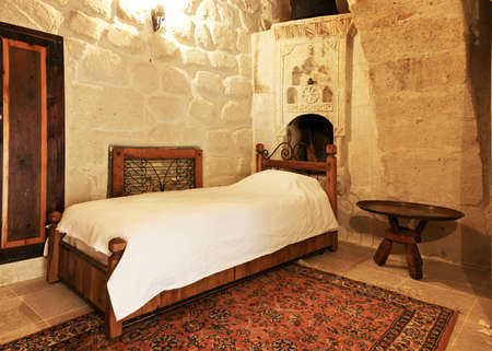 Interior architectural detail of a single persons bedroom, inlaid wardrobe, radiator grill, open fireplace with ornate engraving and motifs, archway, loft space, occasional table and woven mat. Portrait with crop area and copy spaceの写真素材
