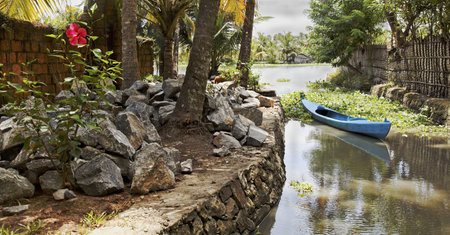 landscape of Kerala backwaters India artery berthed blue canoe local stone granite boulders hybiscus...