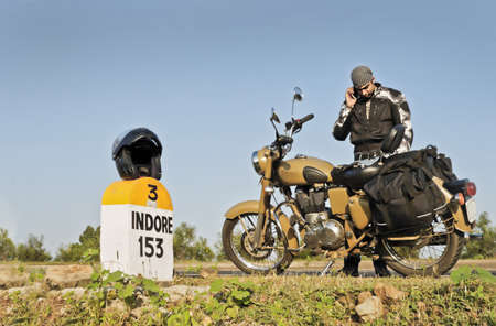 Motorcyclist on an open road in India on his way to Indore using a mobile phone  Helmet on milestone for 153 kilometersの写真素材