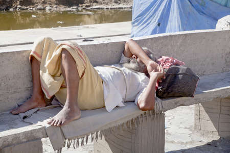 Dwarka Roadtrip Weary foot traveler takes a rest in the blazing heat of the Indian sun on a bench at Bet Dwarka before he completes his pilgrimage at the Hindu temple in Gujarat India の写真素材