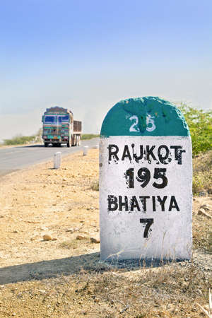 Dwarka Roadtrip  Vertical take of 195 kilometer milestone and direction sign to Rajkot in Gujarat India with a typical truck about to pass by  Rural country side location in the summer season with dry barren wasteland of the regionの写真素材