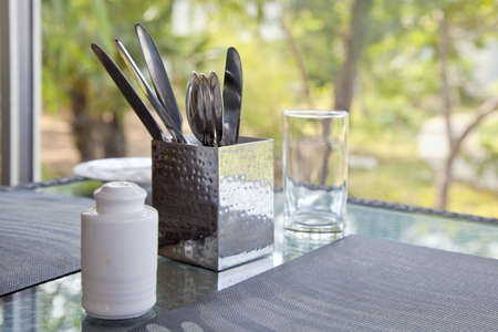 Horizontal capture of a dinner table waiting to be properly set at a picture window looking onto a...