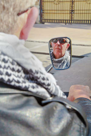 Vertical color portrait of face reflection of a caucasion motorbiker in a rear view mirror waiting at car park gates to open, Generic shot location Bombay India with model releaseの写真素材