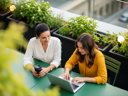 Two young businesswomen working on laptop and drinking coffee in outdoor cafeの素材