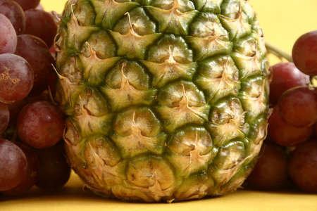 Pineapple and grapes on yellow background の写真素材
