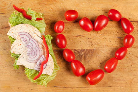 Healthy sandwich with tomatoes arranged in a heart shape on a wooden board.の写真素材