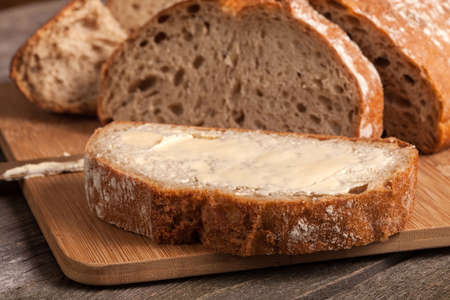 A slice of bread with butter on a chopping board. Selective focus.