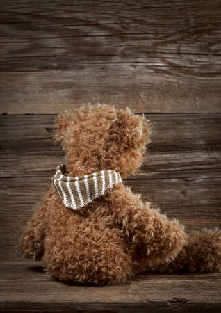 Teddy bear sitting backwards on a wooden table.の写真素材