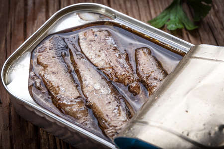 Sprats in oil in a can on a wooden table.