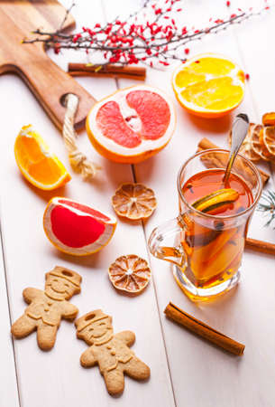 Hot tea with citrus, cinnamon, cloves and honey on a wooden table.