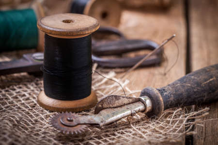 Scissors, bobbins with thread and needles on the old wooden table.の写真素材