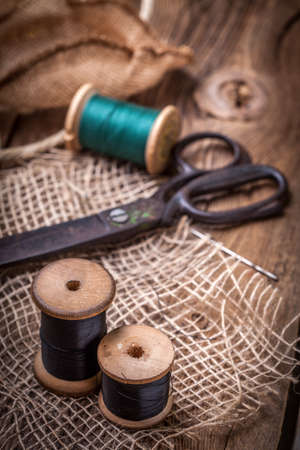 Scissors, bobbins with thread and needles on the old wooden table.