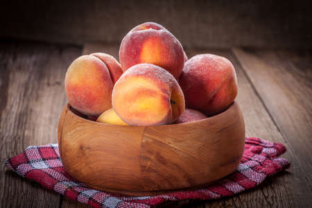 Peaches in a wooden bowl on the tableの写真素材