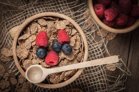 Healthy breakfast - bowl of cereals with blueberries and raspberries on a wooden table.の写真素材
