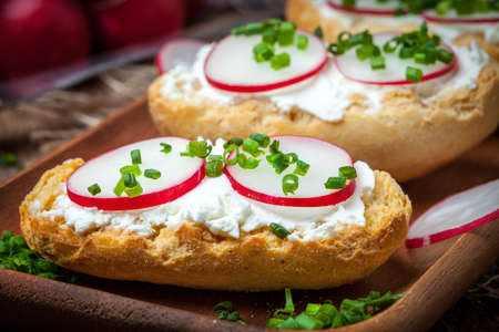 Toasts with radish, chives and cottage cheese on a wooden table. Tasty snack. Selective focus.の写真素材