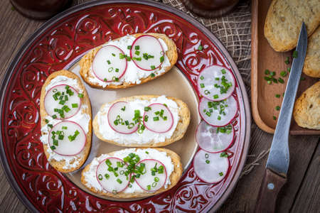 Toasts with radish, chives and cottage cheese on a wooden table. Tasty snack. Selective focus.の写真素材