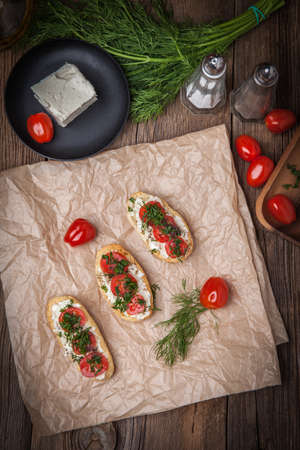 Delicious bruschetta with tomatoes, feta cheese, dill and spice on wooden boardの写真素材