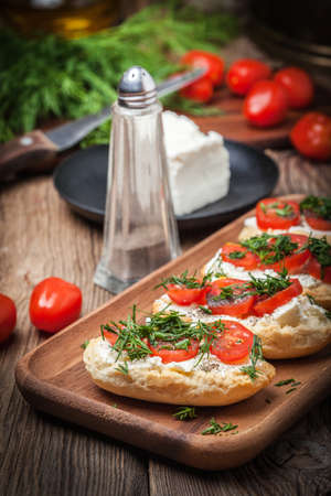 Delicious bruschetta with tomatoes, feta cheese, dill and spice on wooden boardの写真素材